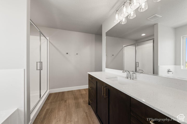 Bathroom with vanity, a shower stall, wood finished floors, a garden tub, and baseboards