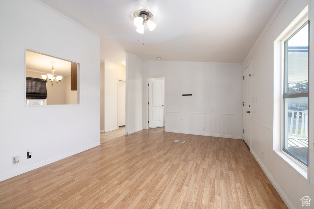 Spare room featuring light wood-type flooring, a chandelier, plenty of natural light, and a ceiling fan