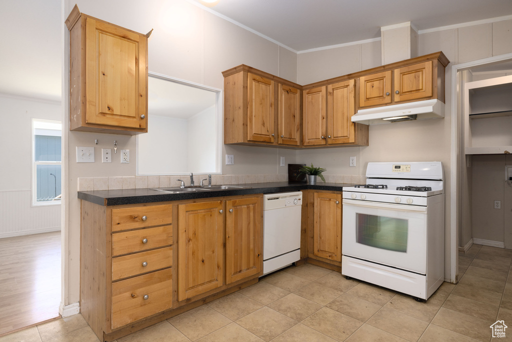 Kitchen with white appliances, under cabinet range hood, a sink, dark countertops, and ornamental molding