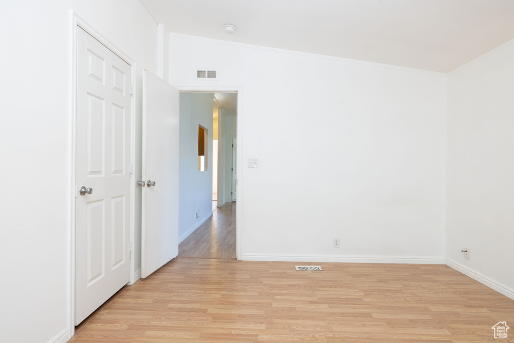 Empty room featuring light wood-style flooring, ornamental molding, and baseboards