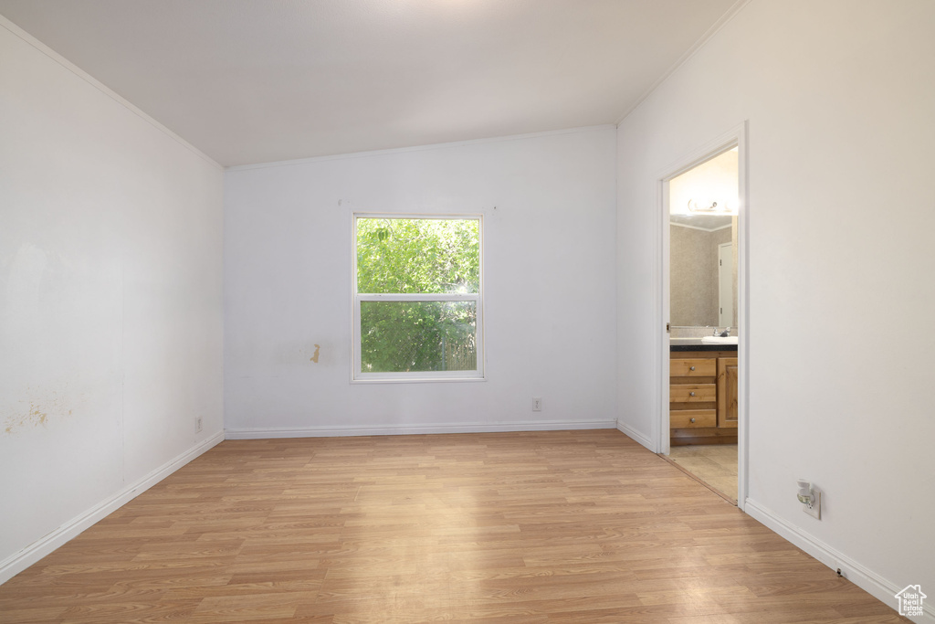 Unfurnished bedroom with light wood-style flooring, crown molding, ensuite bathroom, and baseboards