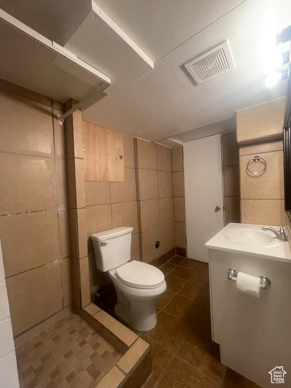 Full bath with vanity, toilet, tile walls, tile patterned floors, and a shower