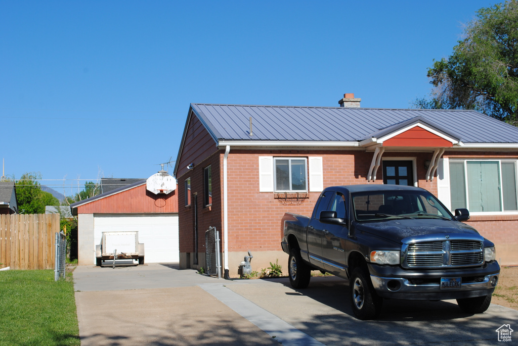 Single story home featuring brick siding, a chimney, metal roof, and a detached garage