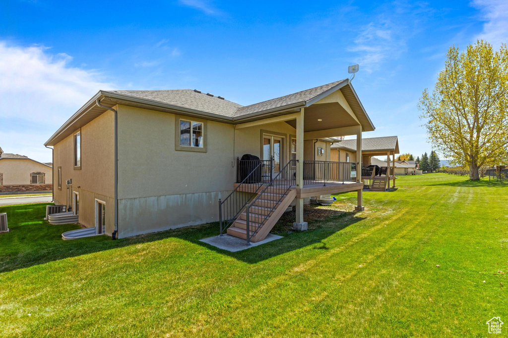 Rear view of property featuring a lawn, stucco siding, a wooden deck, and central AC