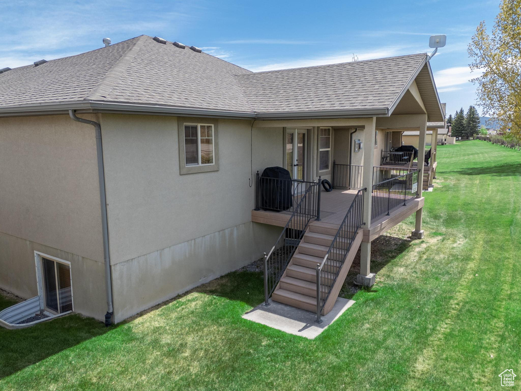 Rear view of property with roof with shingles, a lawn, and stucco siding