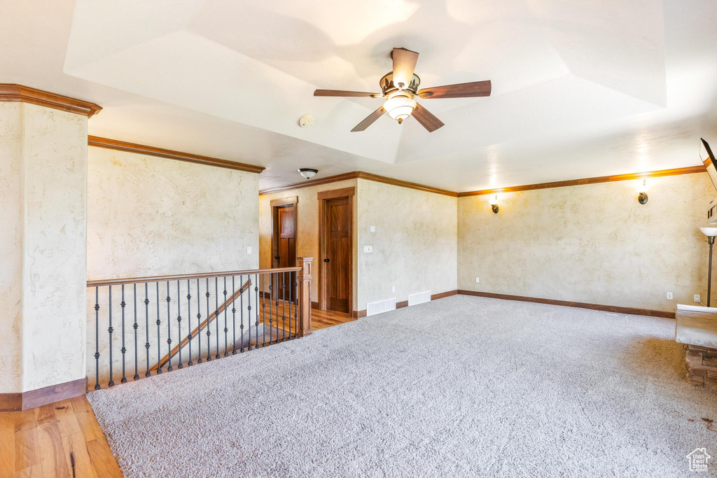 Empty room with ceiling fan, a raised ceiling, a smoke detector, carpet flooring, and ornamental molding