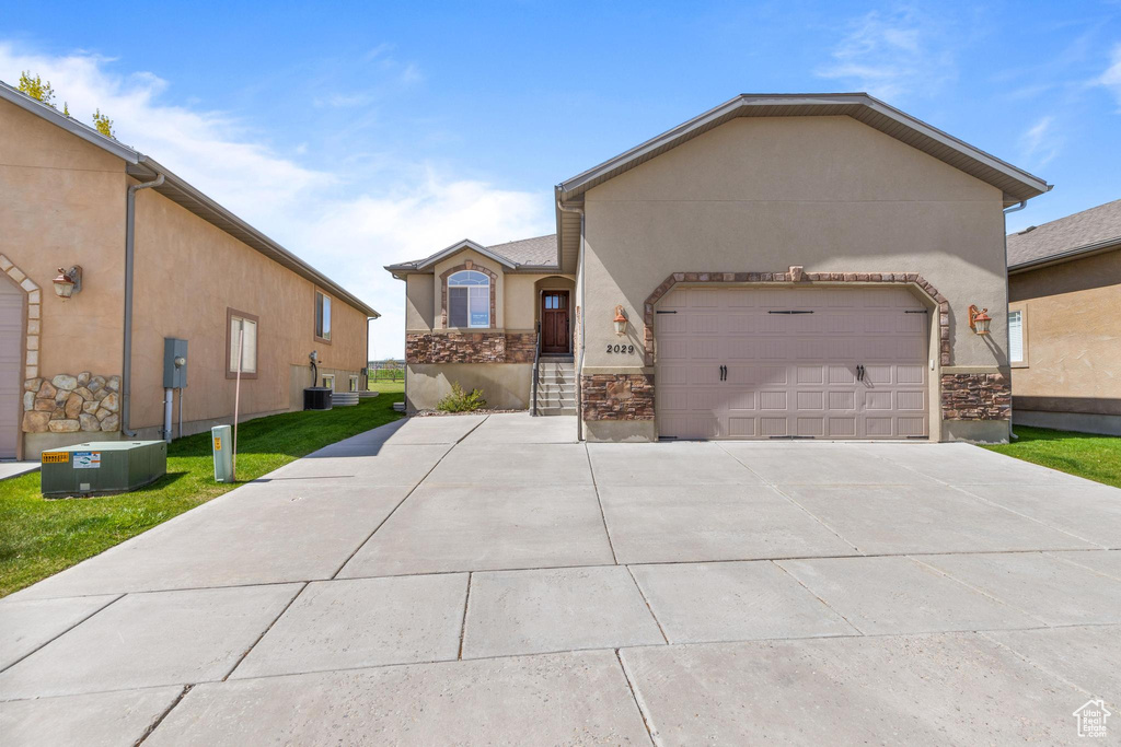 View of front of home with stucco siding, driveway, a garage, stone siding, and central AC unit