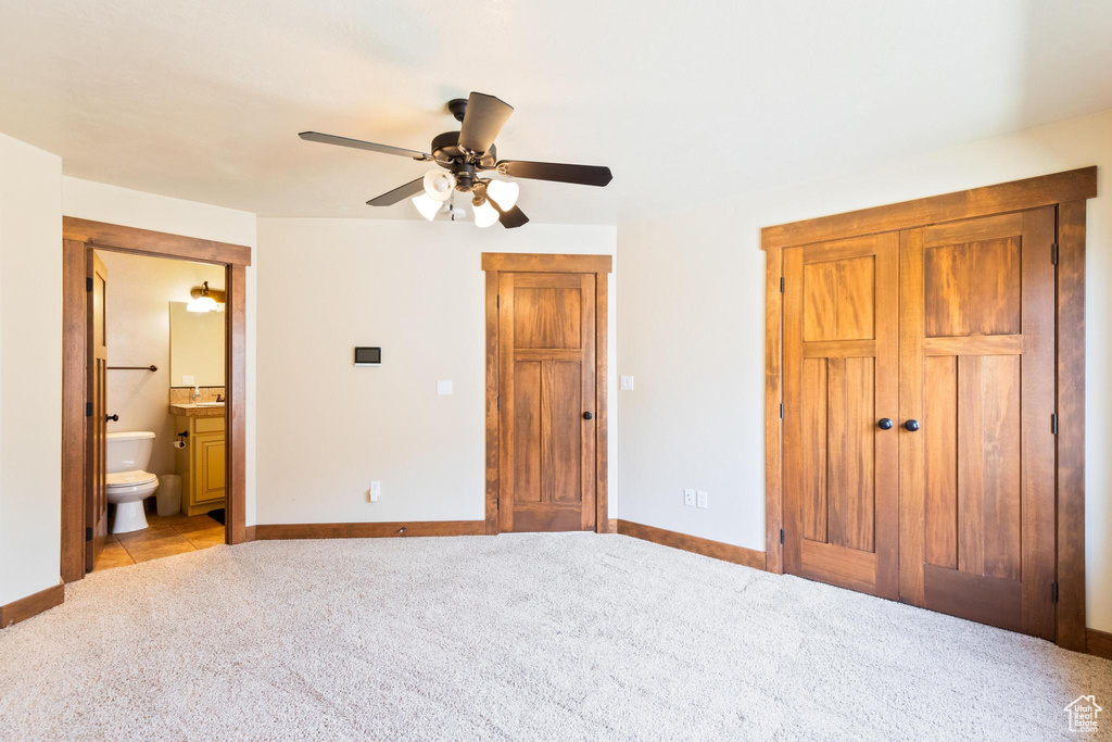 Unfurnished bedroom featuring light carpet, baseboards, ensuite bathroom, and ceiling fan