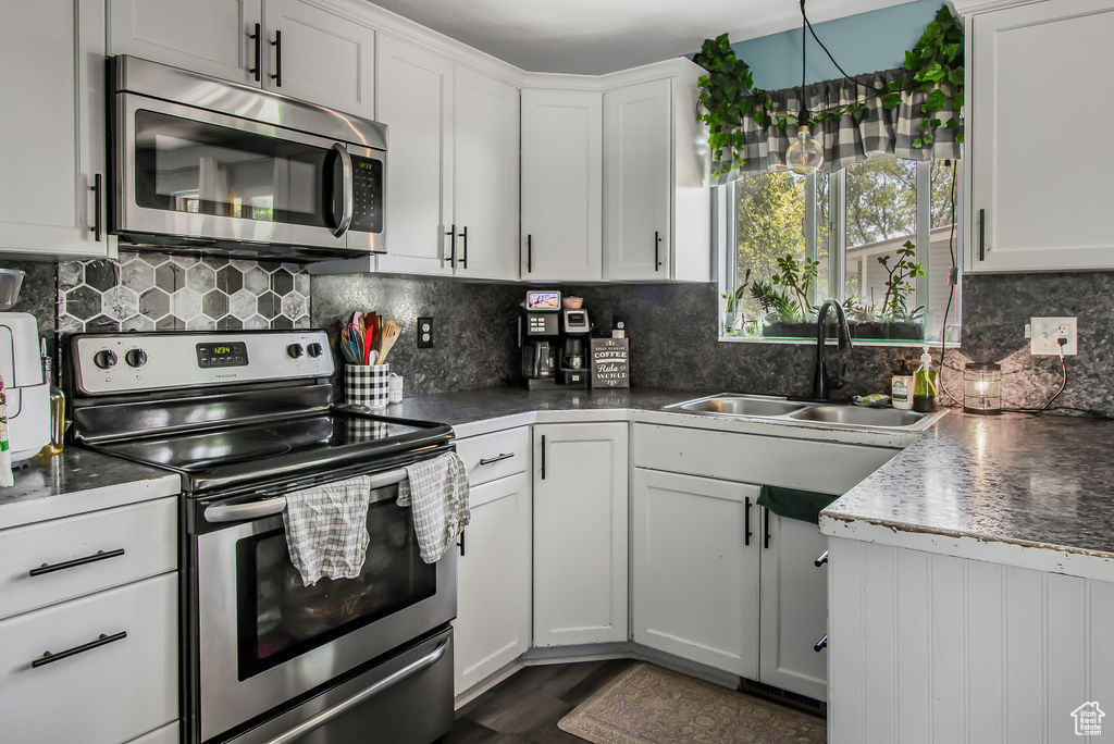 Kitchen with stainless steel appliances, a sink, decorative backsplash, white cabinets, and dark countertops