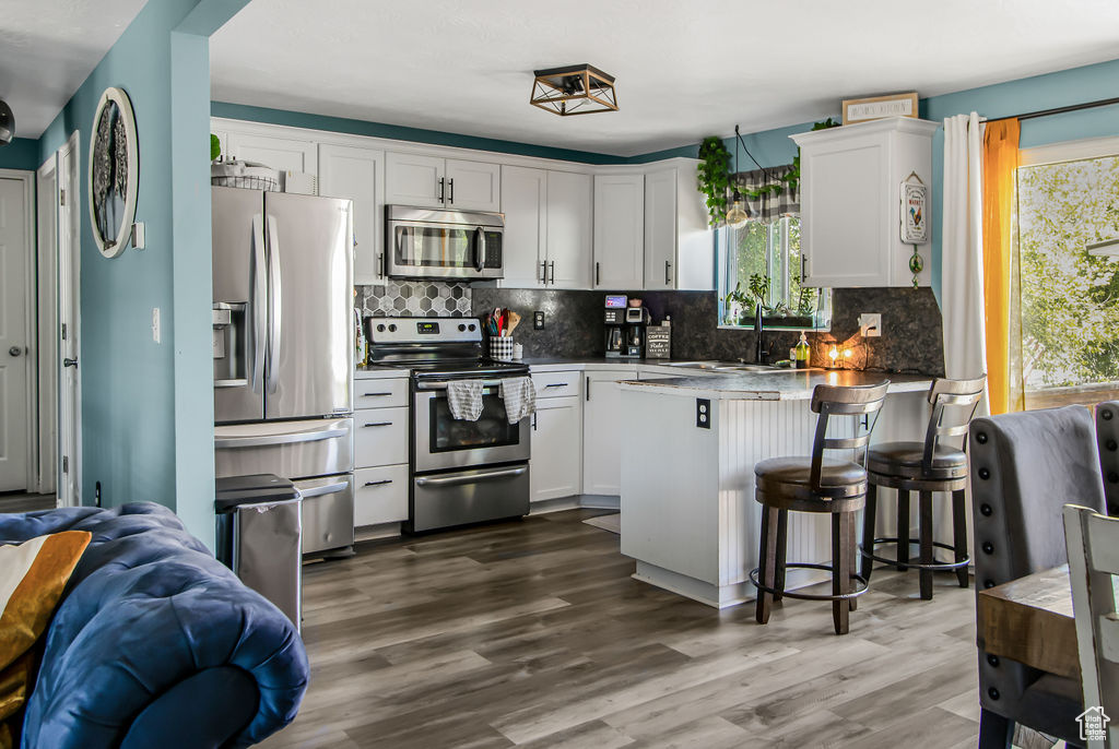 Kitchen with appliances with stainless steel finishes, a sink, a peninsula, white cabinetry, and backsplash