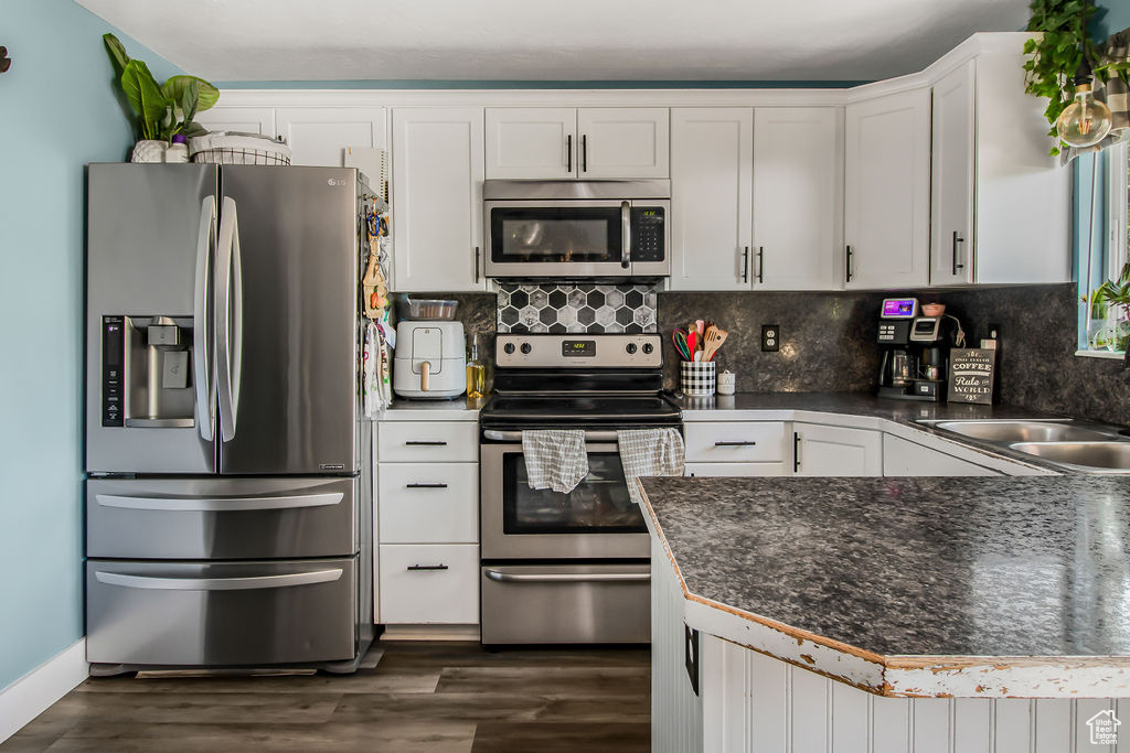 Kitchen with appliances with stainless steel finishes, white cabinetry, dark wood-type flooring, dark countertops, and tasteful backsplash