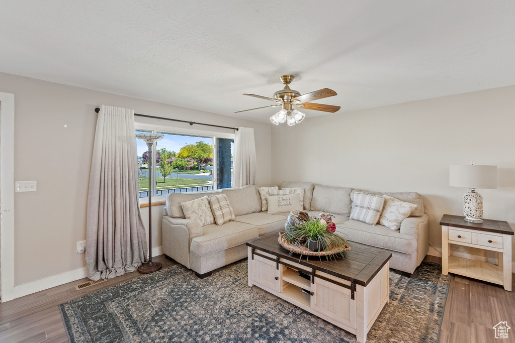 Living area with a ceiling fan, wood finished floors, and baseboards