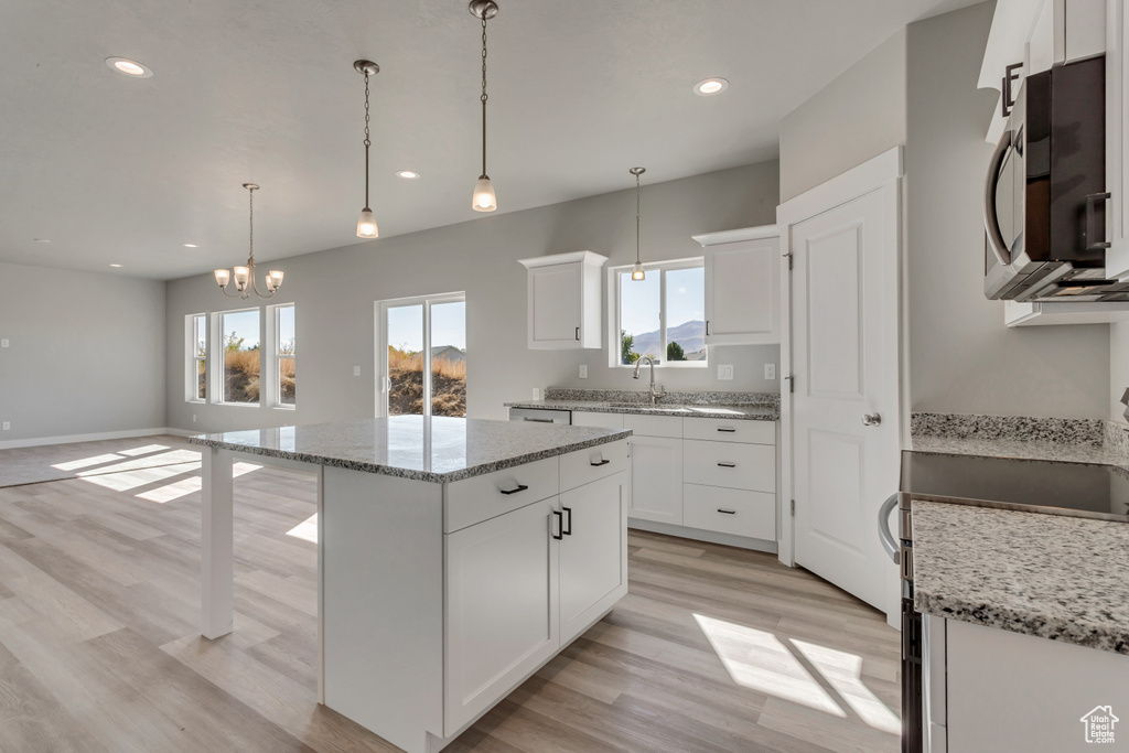 Kitchen with appliances with stainless steel finishes, a kitchen island, a sink, light wood finished floors, and a chandelier