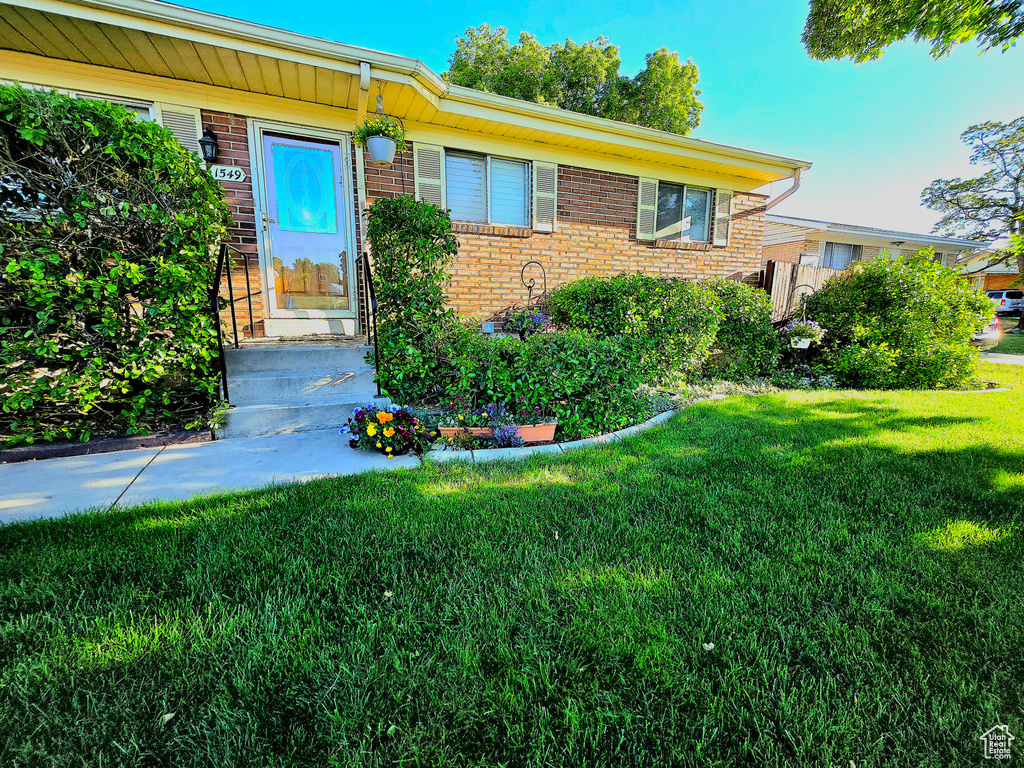 View of exterior entry featuring brick siding and a yard
