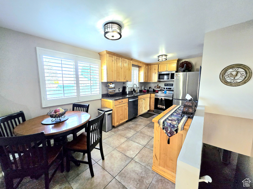 Kitchen featuring appliances with stainless steel finishes, light brown cabinetry, light tile patterned flooring, a sink, and dark countertops