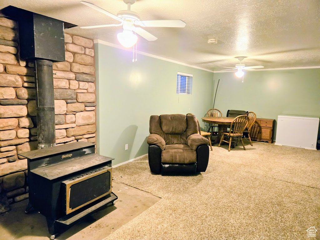 Carpeted living room with a wood stove, ceiling fan, ornamental molding, a textured ceiling, and baseboards