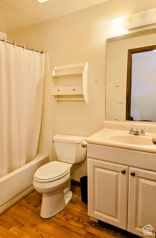 Bathroom featuring wood finished floors, toilet, vanity, shower / tub combo, and a textured ceiling