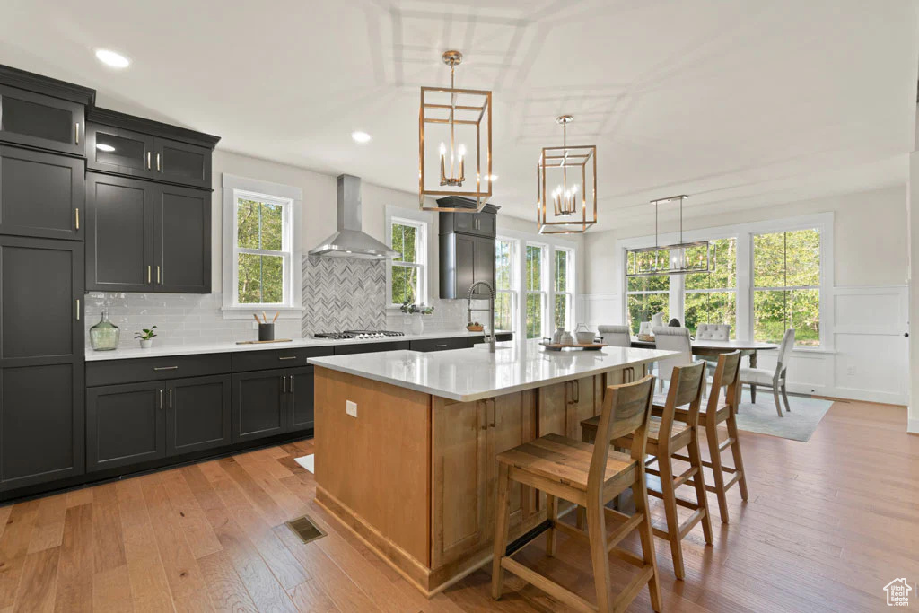 Kitchen with wall chimney range hood, light countertops, gas cooktop, light wood-style flooring, and decorative backsplash