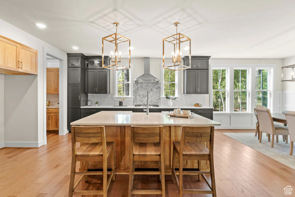 Kitchen with wall chimney range hood, light countertops, light wood-style floors, and recessed lighting