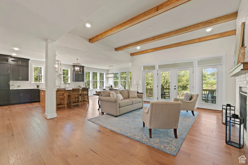 Living room with a fireplace with raised hearth, light wood-style flooring, beam ceiling, a chandelier, and recessed lighting