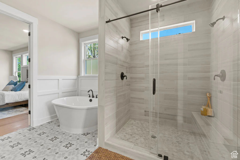 Full bathroom featuring a freestanding tub, a stall shower, connected bathroom, a wainscoted wall, and a decorative wall