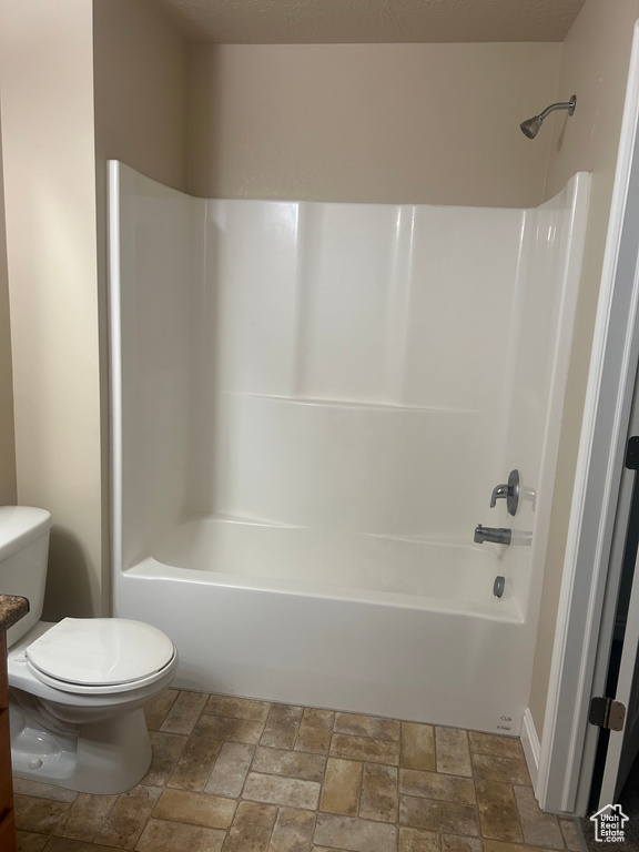 Bathroom with stone tile floors, toilet, and shower / bathtub combination