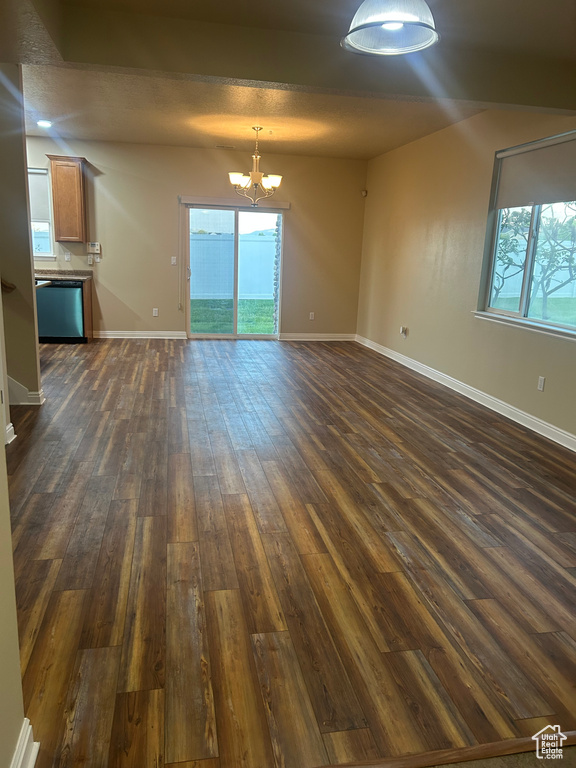 Unfurnished living room featuring a chandelier, dark wood-style flooring, baseboards, and healthy amount of natural light