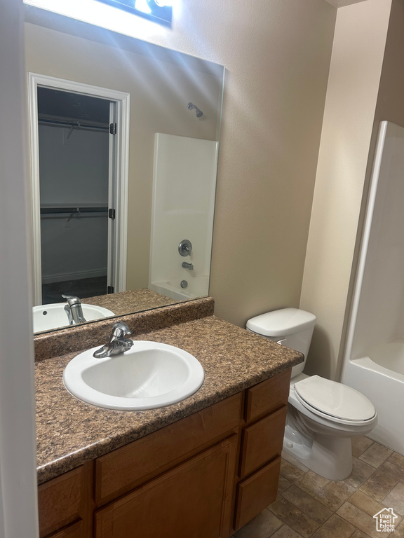 Bathroom with vanity, toilet, a walk in closet, bathing tub / shower combination, and stone finish floors