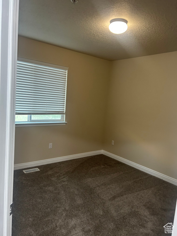 Empty room with dark colored carpet, a textured ceiling, and baseboards