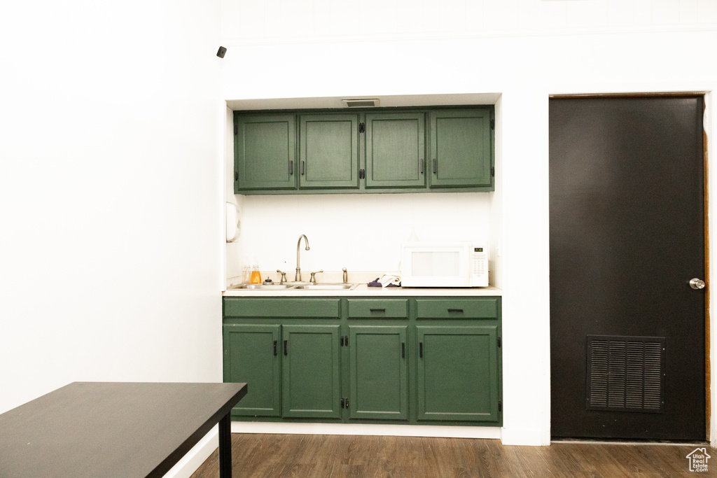 Kitchen featuring green cabinets, white microwave, a sink, and dark wood-style flooring