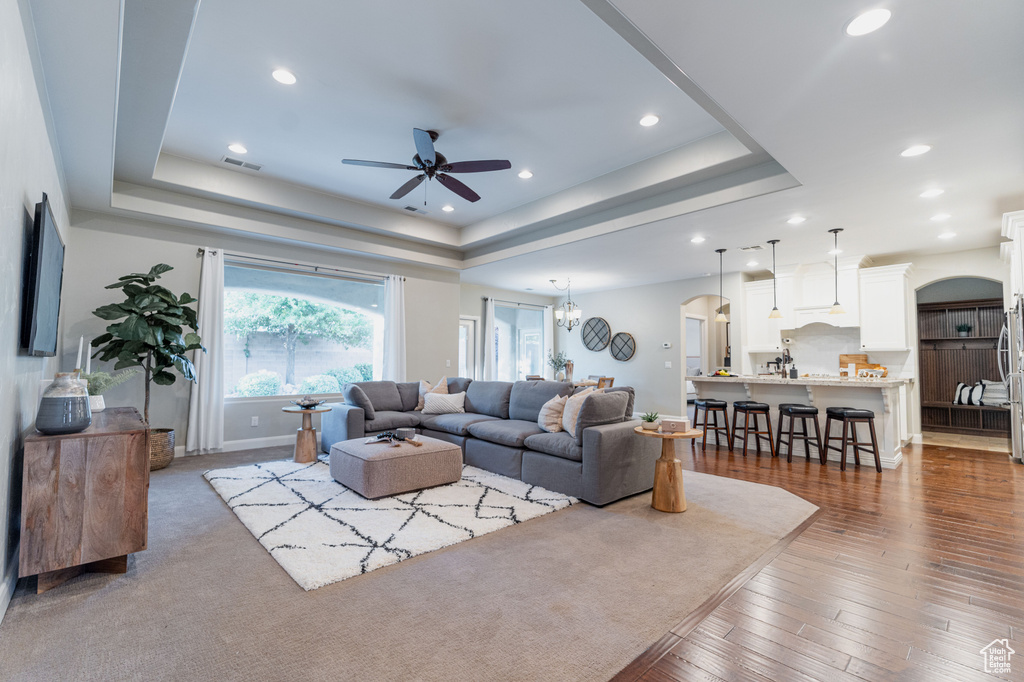 Living area featuring a tray ceiling, a ceiling fan, arched walkways, recessed lighting, and wood finished floors
