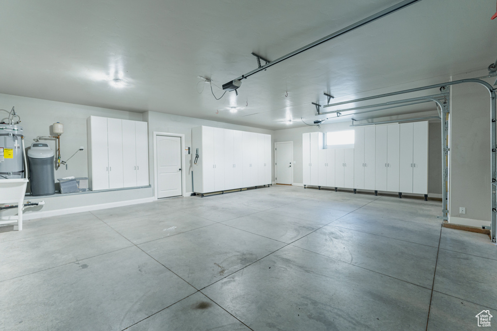 Garage with a garage door opener, baseboards, and electric water heater
