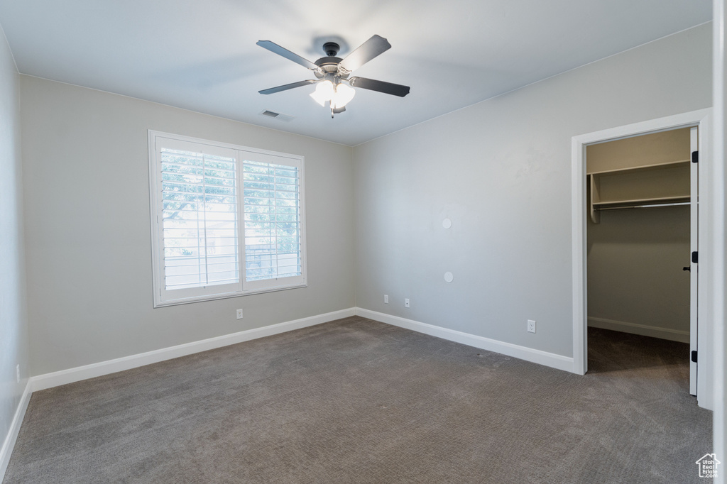 Unfurnished bedroom featuring dark carpet, a walk in closet, baseboards, and a closet