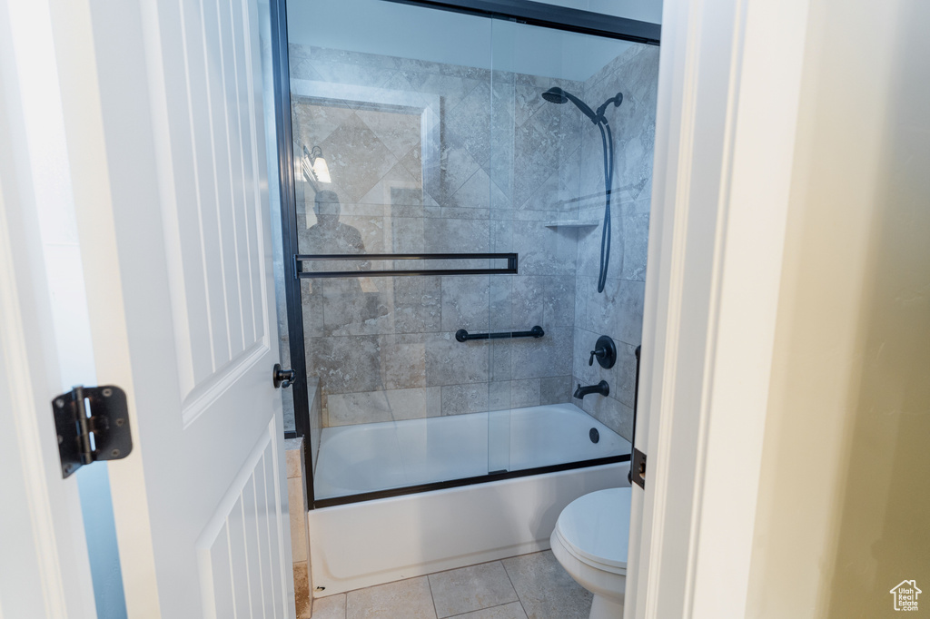 Bathroom with toilet, shower / bath combination with glass door, and tile patterned flooring