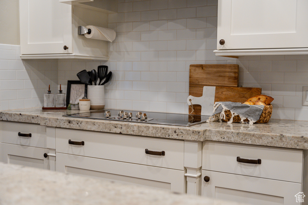 Kitchen featuring backsplash, white cabinetry, black electric stovetop, and light stone counters