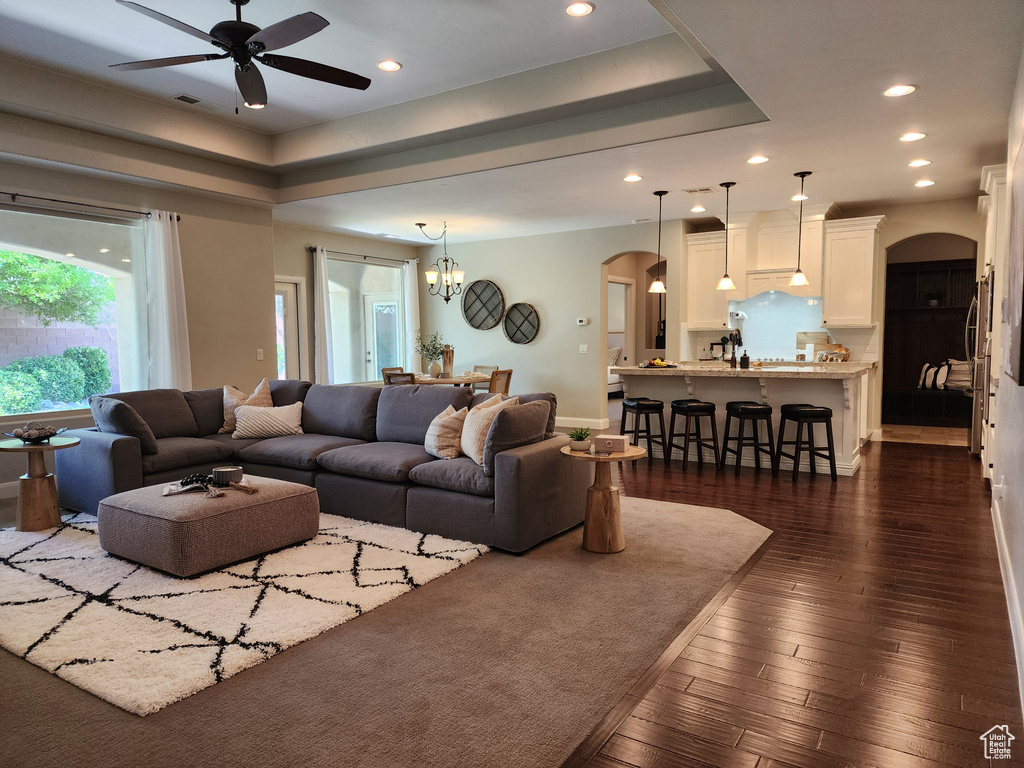 Living area with arched walkways, a ceiling fan, recessed lighting, dark wood-type flooring, and a chandelier