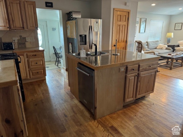 Kitchen with stainless steel appliances, wood finished floors, open floor plan, a sink, and an island with sink