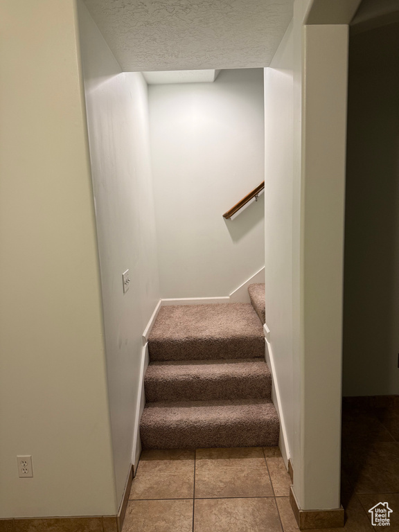 Stairs with baseboards, a textured ceiling, and tile patterned flooring