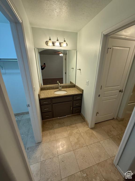 Bathroom with vanity, a textured ceiling, a closet, baseboards, and tile patterned floors