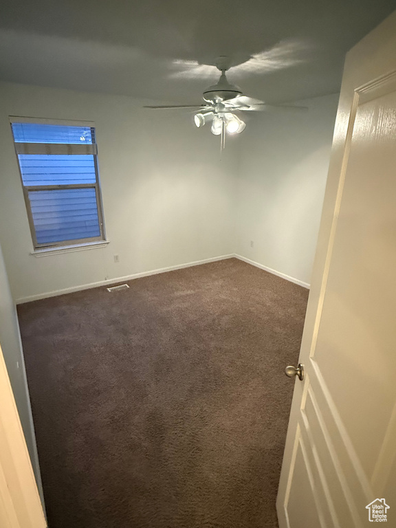 Empty room featuring ceiling fan, dark carpet, and baseboards