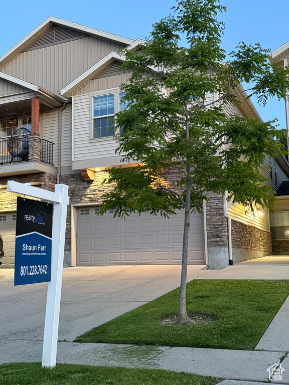View of front of home featuring stone siding, concrete driveway, a balcony, and board and batten siding