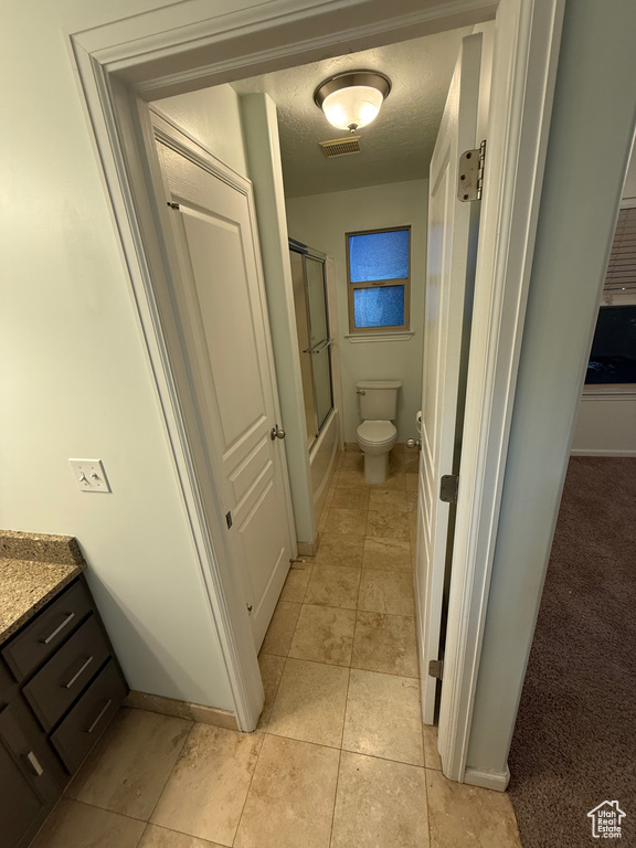 Full bath with tile patterned flooring, vanity, toilet, enclosed tub / shower combo, and baseboards