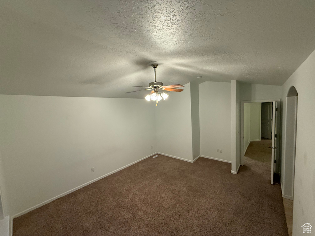 Unfurnished room featuring vaulted ceiling, ceiling fan, dark colored carpet, a textured ceiling, and arched walkways