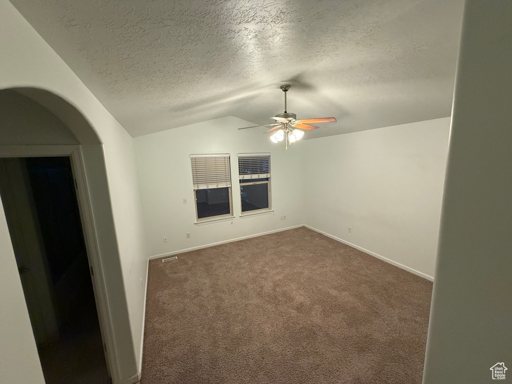 Empty room featuring lofted ceiling, arched walkways, a textured ceiling, a ceiling fan, and dark colored carpet