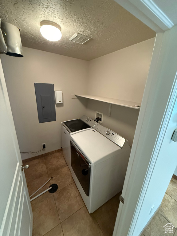 Laundry room featuring electric panel, washing machine and dryer, light tile patterned floors, and a textured ceiling