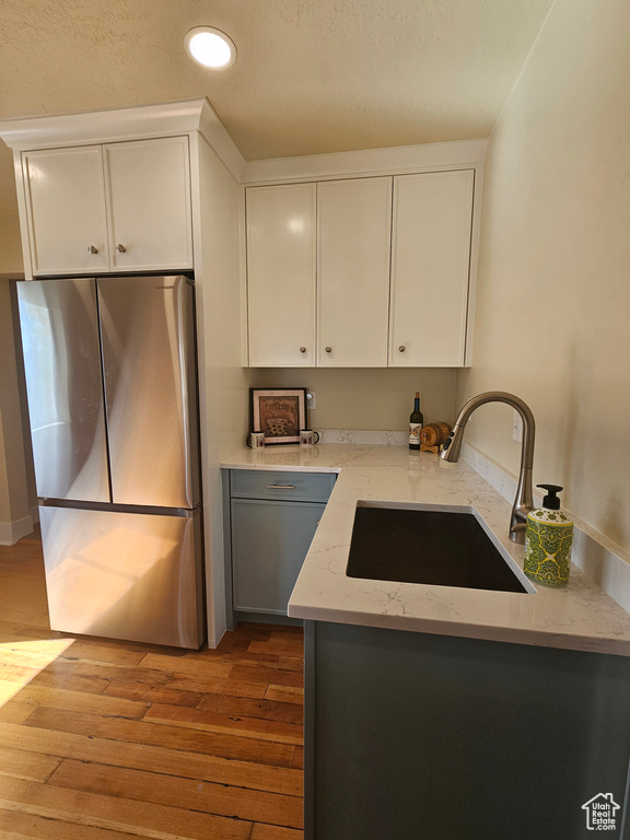Kitchen featuring freestanding refrigerator, a sink, wood finished floors, white cabinetry, and recessed lighting