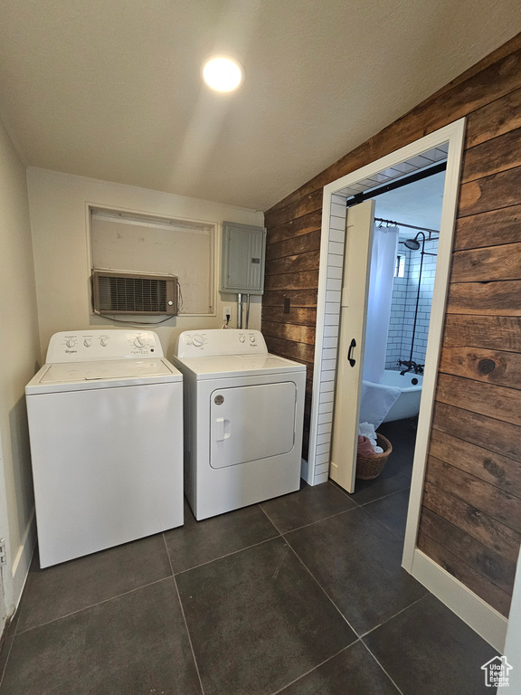 Laundry area featuring washing machine and clothes dryer, dark tile patterned flooring, wood walls, and electric panel