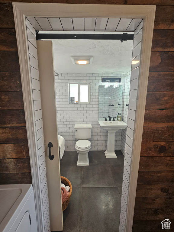 Full bathroom with toilet, washer / clothes dryer, and tile walls