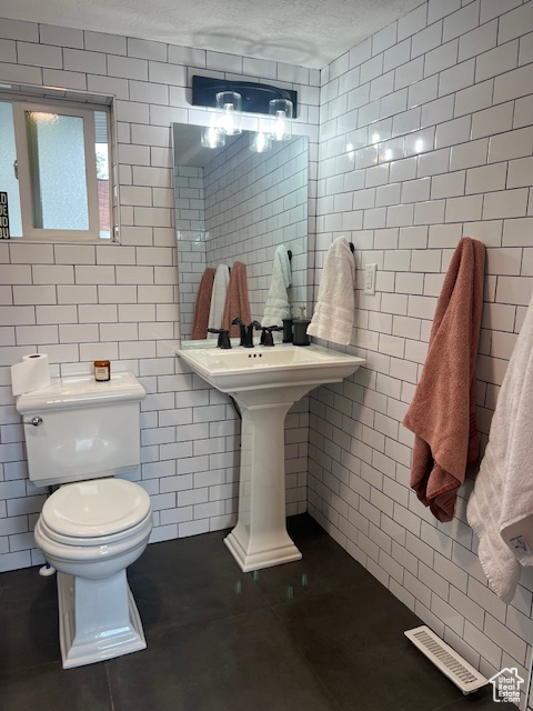 Bathroom featuring tile walls, toilet, tile patterned floors, a textured ceiling, and a sink