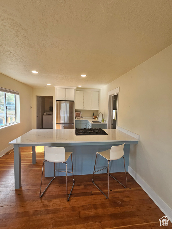 Kitchen featuring stainless steel refrigerator, a sink, a breakfast bar area, washer / dryer, and white cabinets